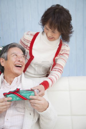 Photo for Asian senior man with gist celebrating Christmas with wife  at home - Royalty Free Image