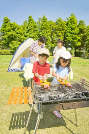 Foto de Feliz joven familia japonesa haciendo barbacoa en el campamento - Imagen libre de derechos