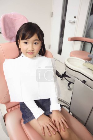 Foto de Pequeña chica japonesa sentado en silla de dentista y mirando a la cámara - Imagen libre de derechos