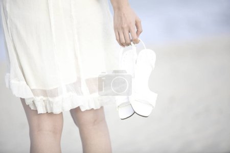 Photo for A woman in a white dress holding a pair of white shoes - Royalty Free Image