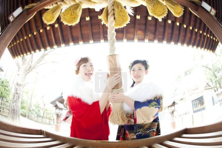 Téléchargez les photos : Filles asiatiques habillées en furisode secouant cloche dans le temple après avoir prié - en image libre de droit