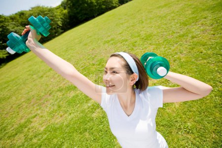 Photo for Woman exercising with dumbbells on lawn - Royalty Free Image