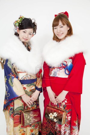 zwei junge asiatische Frauen in traditioneller Kleidung mit Pelzkragen posieren auf weißem Studiohintergrund. traditioneller japanischer Stil
