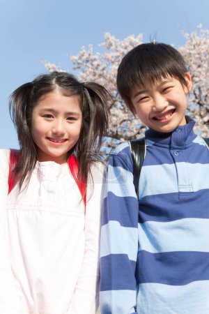 Téléchargez les photos : Enfants japonais souriants avec sacs à dos dans le parc de printemps - en image libre de droit
