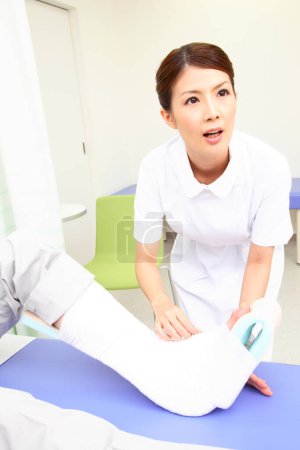 Téléchargez les photos : Asiatique femme infirmière putting gypse sur homme cassé jambe - en image libre de droit