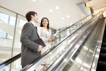 Téléchargez les photos : Deux jeunes hommes et femmes d'affaires sur escalator - en image libre de droit