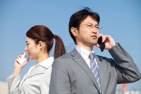 Téléchargez les photos : Un homme et une femme en tenue de travail parlant sur des téléphones portables - en image libre de droit