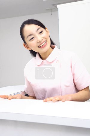 Photo for Smiling Japanese receptionist behind counter in dental office - Royalty Free Image