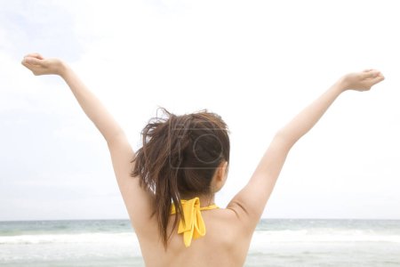 Foto de Mujer asiática con los brazos extendidos de pie en la playa, vista trasera - Imagen libre de derechos