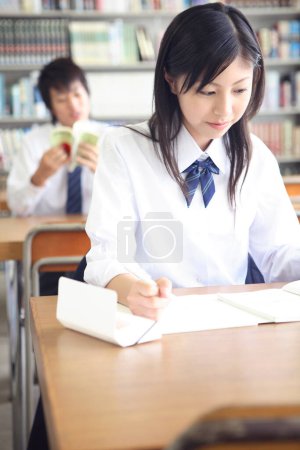 Téléchargez les photos : Jeune écolière japonaise étudiant dans la bibliothèque - en image libre de droit