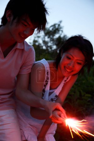 Photo for Happy Japanese man and woman with sparkler in evening - Royalty Free Image