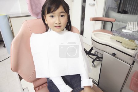 Photo for Little Asian girl sitting in dentist chair and looking at camera - Royalty Free Image