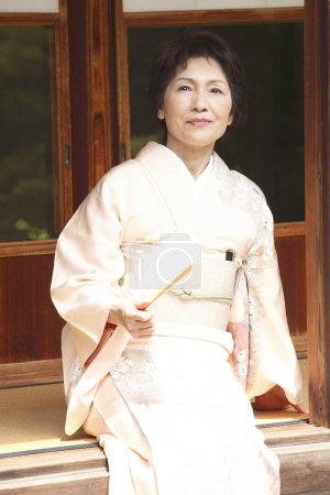 Téléchargez les photos : Belle femme japonaise mature avec ventilateur pliant assis sur engawa - en image libre de droit