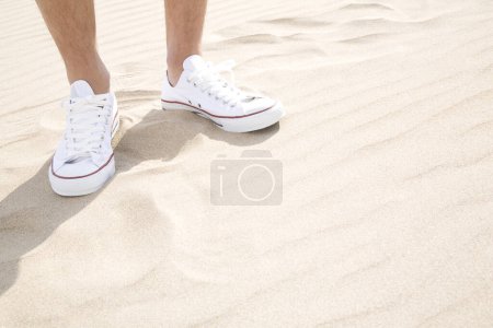 Téléchargez les photos : Photo recadrée de jambes masculines en baskets blanches debout sur la plage - en image libre de droit