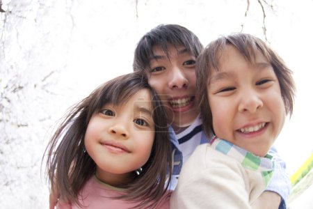 Photo for Happy asian family of three with blooming cherry tree on background - Royalty Free Image