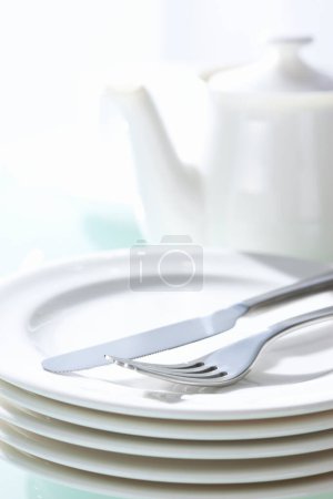Foto de Tetera, platos blancos, tenedor y cuchillo sobre fondo de mesa - Imagen libre de derechos