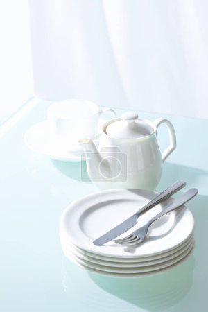 Photo for Tea pot,  white plates, fork and knife  on table  background - Royalty Free Image