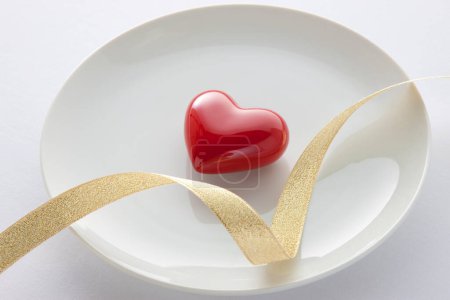 Photo for Red heart with ribbon on white plate - Royalty Free Image