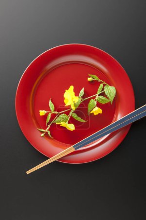 Photo for Top view of yellow flowers in red plate and chopsticks on black background - Royalty Free Image