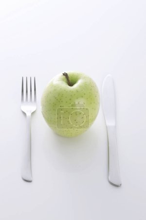 Téléchargez les photos : Concept de régime, pomme verte sur une assiette blanche, fourchette, couteau - en image libre de droit