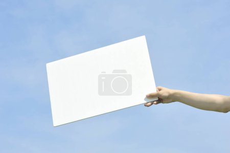 Téléchargez les photos : Main tenant une bannière blanche vierge sur fond de ciel - en image libre de droit