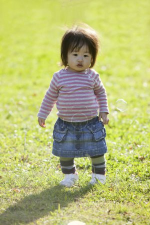 Téléchargez les photos : Mignonne asiatique fille jouer avec savon bulles sur l herbe dans le parc - en image libre de droit