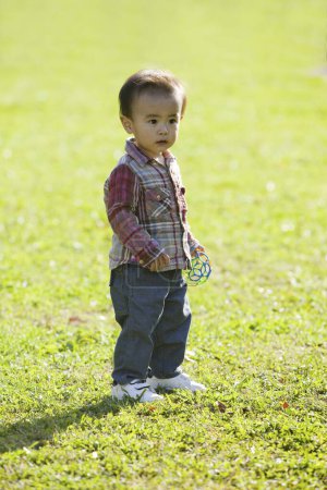 Téléchargez les photos : Mignon asiatique garçon jouer sur l 'herbe dans parc - en image libre de droit