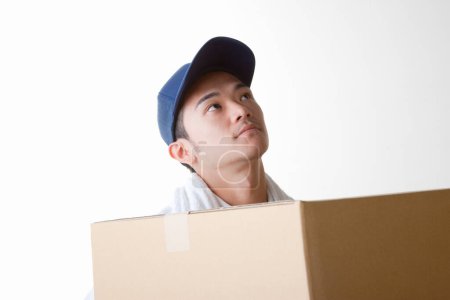 Téléchargez les photos : Livreur fatigué avec boîte en carton dans l'entrepôt - en image libre de droit