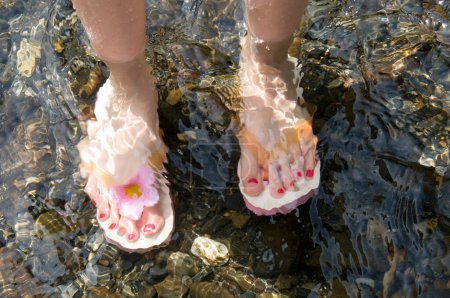Photo for Female Feet Wearing Flip-Flops In The Water - Royalty Free Image