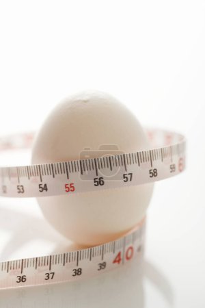 Photo for A closeup shot of a white egg with measuring tape on a white background - Royalty Free Image