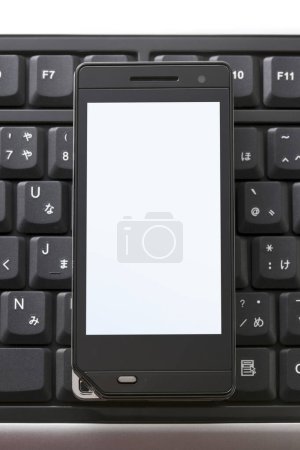 Photo for Smartphone positioned on top of a computer keyboard, ready for use. - Royalty Free Image