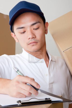 Photo for Young asian delivery man writing on clipboard - Royalty Free Image
