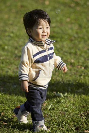 Foto de Lindo asiático chico jugando en la hierba en el parque - Imagen libre de derechos