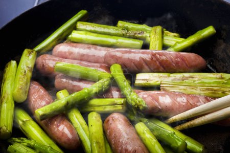 Photo for Sausages and green Asparagus cooking in frying pan - Royalty Free Image