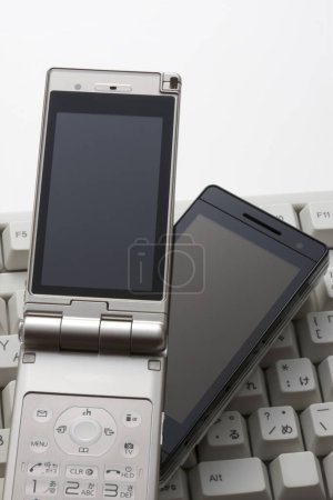 Téléchargez les photos : Smartphone placé sur un clavier d'ordinateur, prêt à l'emploi. - en image libre de droit