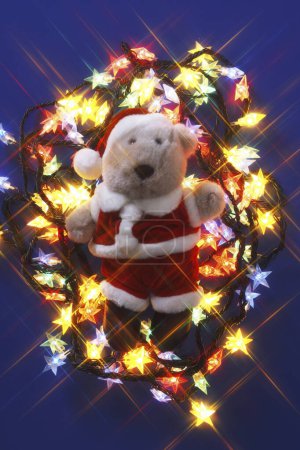 Photo for Christmas teddy bear wearing santa claus costume and electric garland - Royalty Free Image