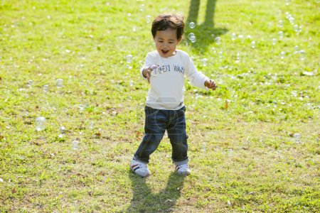 Foto de Lindo asiático chico jugando con jabón burbujas en la hierba en el parque - Imagen libre de derechos