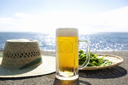 Photo for Beer with green peas and straw hat on seashore background - Royalty Free Image