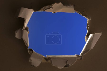 Téléchargez les photos : Trou dans du papier déchiré sur fond bleu - en image libre de droit