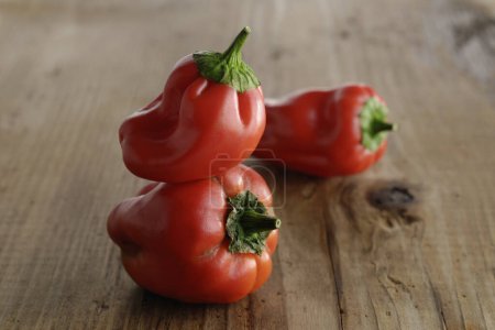 Photo for Three red peppers sitting on a wooden table - Royalty Free Image