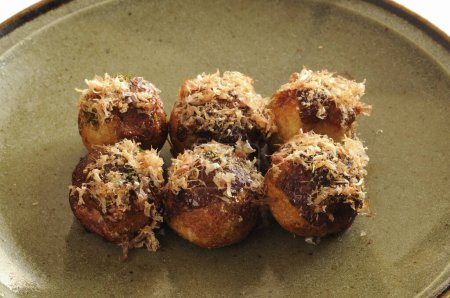 Takoyaki, ball-shaped Japanese snacks made of a wheat flour-based batter and cooked in a special molded pan. It is typically filled with minced or diced octopus, tempura scraps, pickled ginger, and green onion 