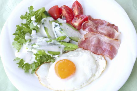 Téléchargez les photos : Œufs, bacon, légumes et pain grillé sur une assiette blanche sur la table. - en image libre de droit