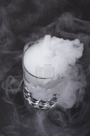 Téléchargez les photos : Fumée blanche en verre avec l'effet de la glace sèche sur fond sombre - en image libre de droit