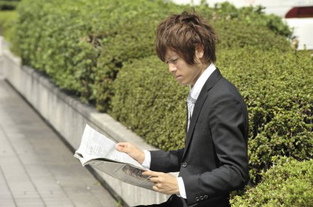 Foto de Asiático joven empresario leyendo periódico en parque - Imagen libre de derechos