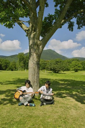 Téléchargez les photos : Deux hommes asiatiques jouant avec guitare et batterie dans le parc - en image libre de droit
