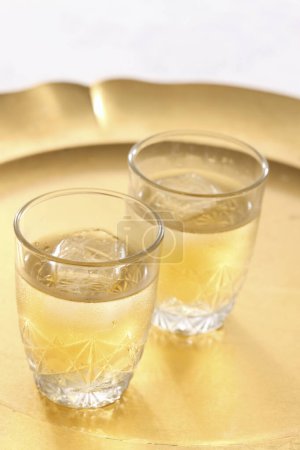 Photo for Glasses of gold and silver tea with ice on a light table - Royalty Free Image