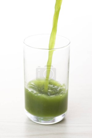 Photo for Close-up view of green fresh healthy organic drink pouring in glass on light background - Royalty Free Image