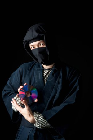 Téléchargez les photos : Jeune homme en costume ninja tenant un disque compact - en image libre de droit