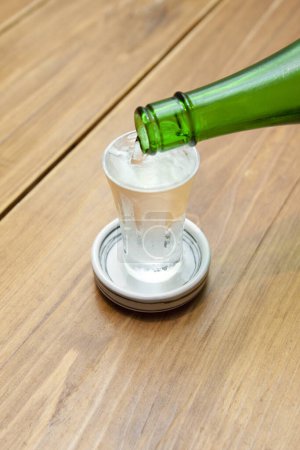 Sake poured into glass from bottle on background, close up