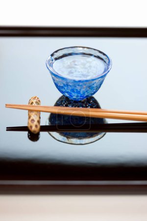 Photo for Close up view of chopsticks placed on resting base and cup of sake - Royalty Free Image